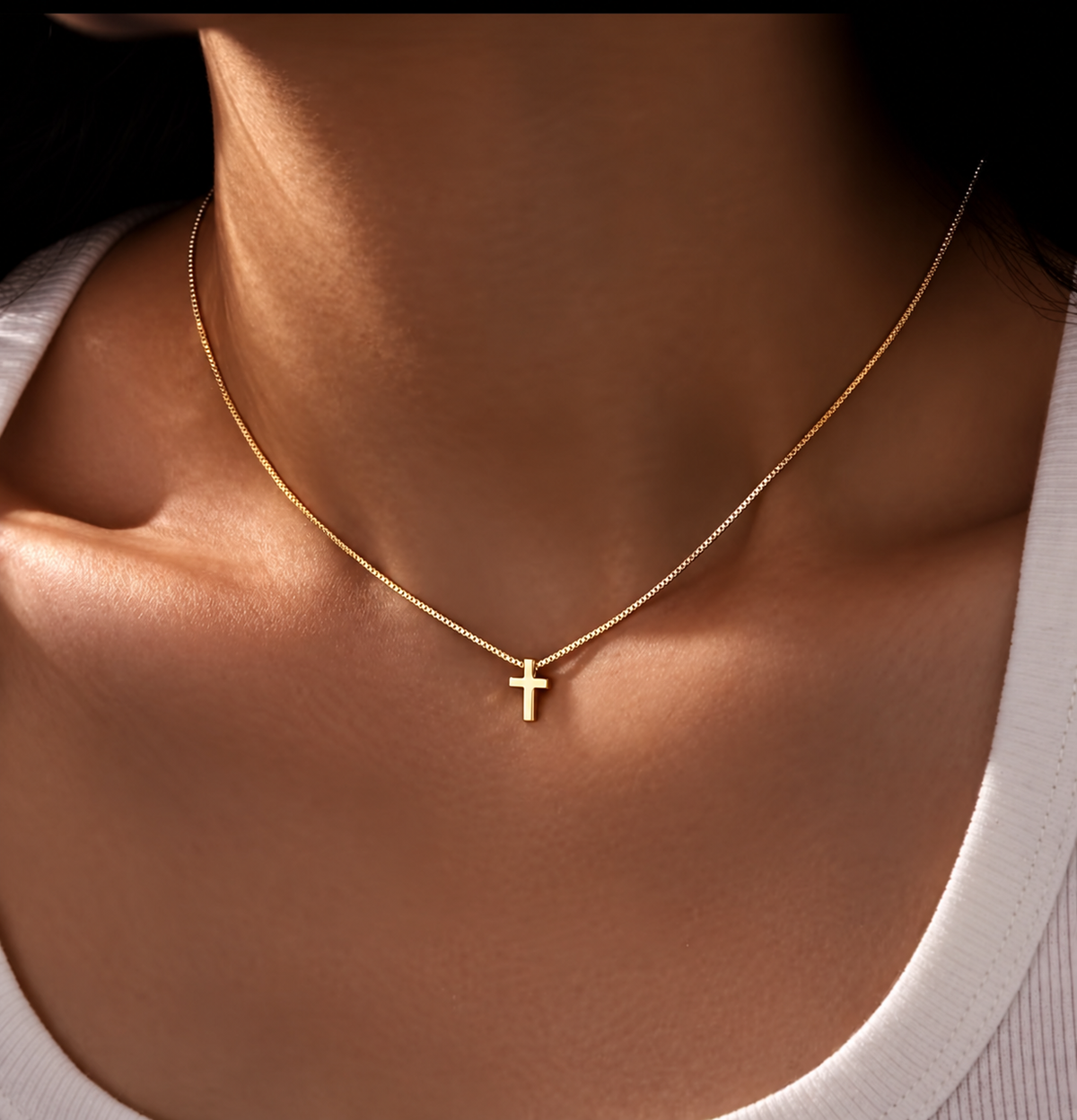 Collar dorado con colgante de cruz fina, usado por modelo; foto limpia sin textos.