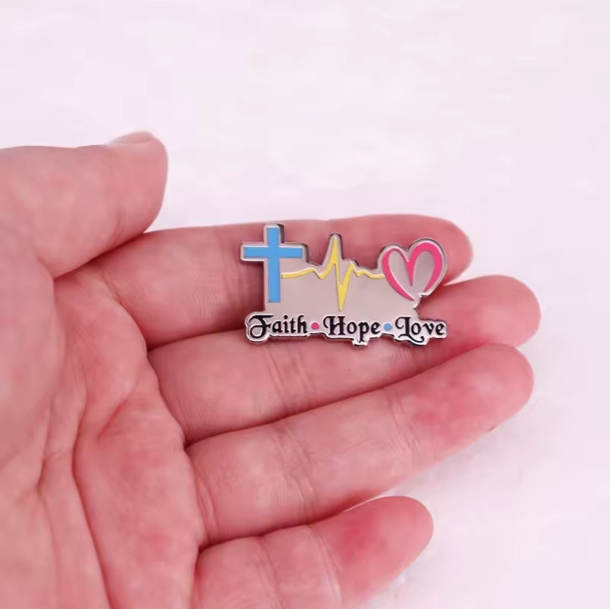 Pin cristiano Fe Esperanza Amor mostrado en la mano para referencia de tamaño