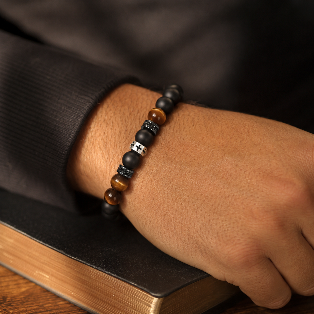 Pulsera Cruz en Ojo de Tigre puesta en muñeca de hombre junto a una Biblia